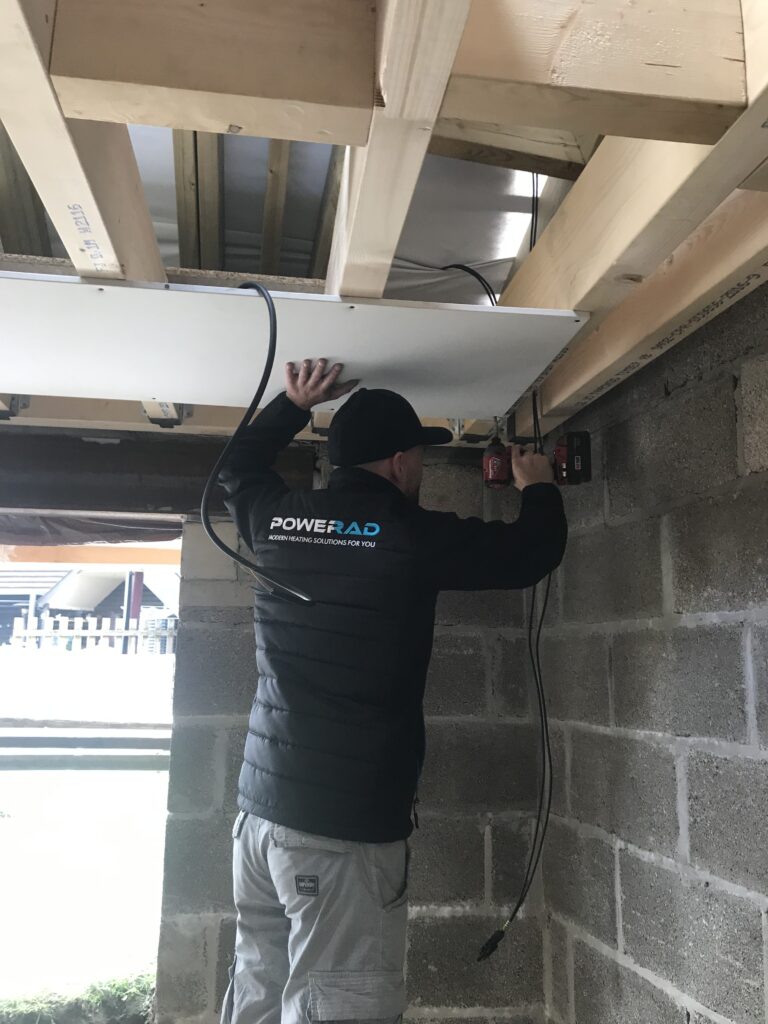 A PoweRad installer fitting a PowerBoard infrared ceiling panel